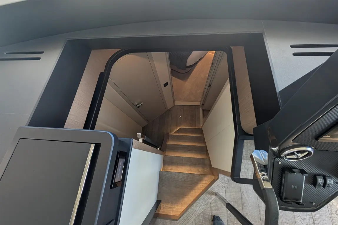 View from above a staircase descending into a modern boat interior, featuring wooden steps and contemporary decor.